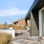 Deck with lounge, table, and chairs. Background: dunes and vacation home.