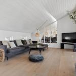 Living room with gray sofa, wooden floor, and white ceiling. TV and plant are visible.