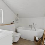 Bathroom with freestanding bathtub, toilet, and sink under sloped ceiling.