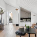 Living area with sleeping nook, sofa, and table. Wooden floor and white walls.