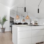 Modern kitchen with white cabinets and kitchen island. Hanging lamps and plant are visible.