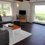 Wohnzimmer mit Sofa, Couchtisch und TV. Balkon mit Blick auf Feld.