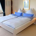 Doppelbett mit blauen Kissen und weißen Bettwäsche. Fenster mit dunklen Vorhängen und Nachttisch mit Lampe.