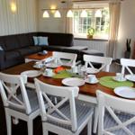 Esszimmer mit Holztisch, weißen Stühlen und dunklem Sofa im Hintergrund.