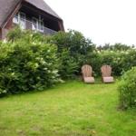 Garten mit zwei Holzstühlen, Grasfläche und Sträuchern vor einem Haus mit Balkon.