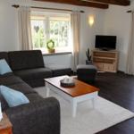 Wohnzimmer mit Sofa, Couchtisch und TV. Fenster und Terrassentür mit Blick.