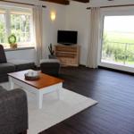 Wohnzimmer mit Sofa, Couchtisch und TV. Balkon mit Blick auf Feld.