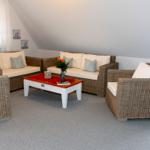 Wohnzimmer mit Rattanmöbeln, weißem Tisch und Blumen.