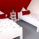 Zwei weiße Einzelbetten mit rosafarbenem Bettzeug und roten Kissen.