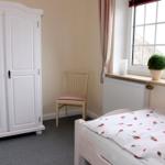 Schlafzimmer mit Bett, Kleiderschrank und Stuhl. Fenster mit Pflanze und Deko.