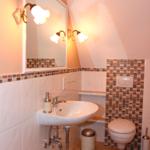 Badezimmer mit Waschbecken, Toilette und Spiegel mit Beleuchtung.