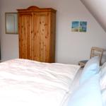 Schlafzimmer mit Dachschräge, Holzschrank und Bett mit weißen Laken.