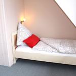 Ein Bett mit Blumenbezug und rotem Kissen unter einem Dachfenster mit rotem Vorhang.