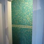 Duschkabine mit grün-gelben Mosaikfliesen und weißem Bogenrahmen.