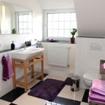 Badezimmer mit Waschbecken, Toilette und Duschbereich. Schwarze und weiße Fliesen.