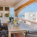 Terrasse mit Tisch und Stühlen, Blick auf das Meer und moderne Gebäude.