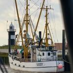 Fischerboot Claudia Wremen liegt im Hafen vor einem Leuchtturm.