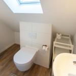 Badezimmer mit Toilette, Waschbecken und Dachschräge mit Dachfenster.