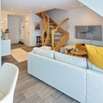 Wohnzimmer mit Sofa, Fernseher und Holztreppe. Küche und Flur sind sichtbar.