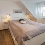 Schlafzimmer mit Dachschräge, Bett, Fenster und Wanddekoration.