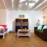 Wohnzimmer mit Sofa, Bett und Holzboden. Decke mit Balken.