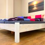 Ein Bett mit Holzrahmen, bunten Kissen und einer Wanddekoration.