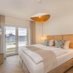 Schlafzimmer mit Doppelbett, TV und Balkonansicht.