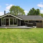 Ein Haus mit Terrasse, Grill und Garten unter blauem Himmel.