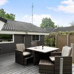 Terrasse mit Sitzgruppe, Tisch und Grill. Hintergrund: Holzhaus und Grünflächen.