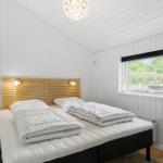 Schlafzimmer mit Bett, Holzwand und Fenster. Gelber Nachttisch und Decken.