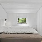 Schlafzimmer mit weißem Bett und Fenster zum Wald.