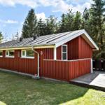 Rotes Holzhaus mit Terrasse und Garten. Umgeben von Bäumen unter blauem Himmel.