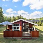 Roter Holzhaus mit Terrasse und Garten unter blauem Himmel.
