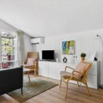 Wohnzimmer mit schwarzen Sofas, Holzstühlen und Fernseher an weißer Wand.