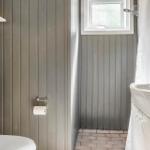 Badezimmer mit Toilette, Waschbecken und Dusche. Holzwand und Fenster sichtbar.