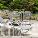 Terrasse mit Liegestühlen, Tisch und Stühlen, umgeben von Gräsern und Bäumen.