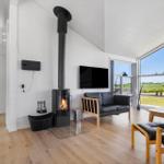Wohnraum mit Kamin, Sofa und großem Fenster mit Blick auf Felder.
