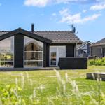 Moderne Villa mit großem Garten und Glasfassade. Terrasse und Satellitenschüssel sichtbar.