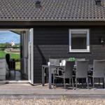 Schwarzes Haus mit Terrasse, Tisch und Stühlen. Durchgehendes Fenster zur Küche.