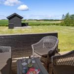 Terrasse mit Sitzgelegenheit und Blick auf grünes Feld und kleines Haus.