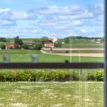 Aus dem Fenster sieht man grüne Felder, eine Kirche und einige Häuser.