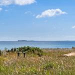 Grasland mit Holztisch und Strandkorb, Blick auf das Meer und eine Insel.