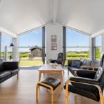 Wohnzimmer mit schwarzen Ledersofas, Holztisch und großem Fensterblick auf die Landschaft.