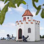 Eine weiße Kapelle mit rotem Dach, Fahrräder und Kinderwagen vor Ort.
