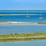 Sailboats and people on a sandy beach near calm blue water.