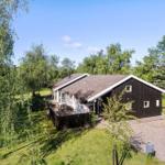 Ein Haus mit dunkler Fassade und weißem Dachrand, umgeben von Bäumen und Gras.