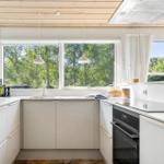 Küche mit weißen Schränken und Fenstern zum Garten