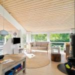 Wohnraum mit Holzdecke, Sofa, Kamin und großen Fenstern.