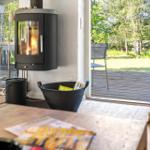 Wohnzimmer mit Kamin, Holzterrasse und Blick auf Grünflächen.