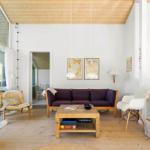 Wohnzimmer mit Sofa, Tisch und Sesseln. Holzdecke und Fenster zur Terrasse.